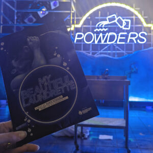 Programme for My Beautiful Laundrette in front of a neon sign that says Powders. 