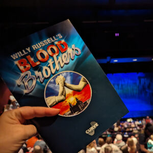 Programme cover for Blood Brothers musical in front of blue-lit stage