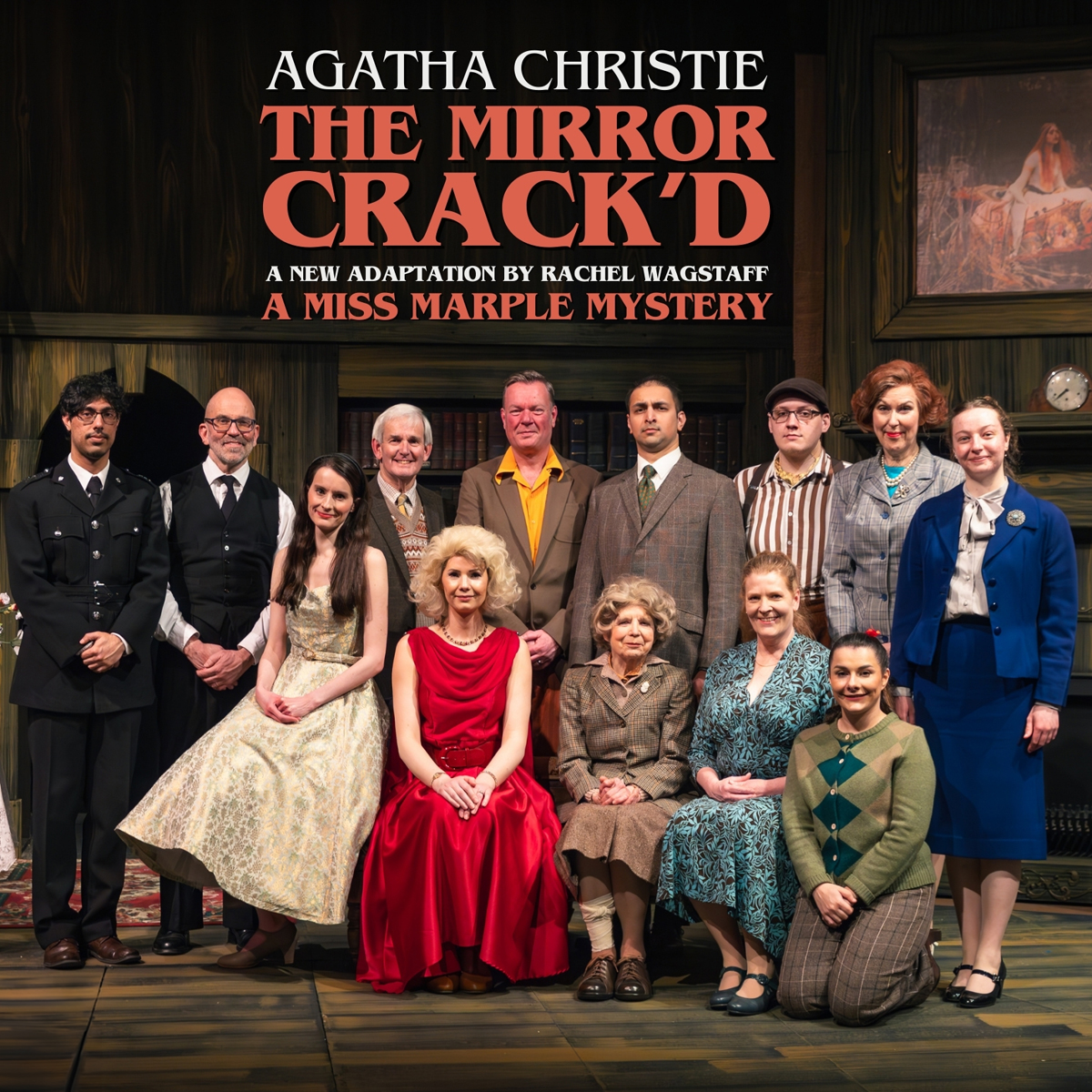 A group of people in 1950s style clothing posed for a formal photograph. There are two rows with the back row standing and the front row seated. They are under a header dominated by the words "The Mirror Crack'd".